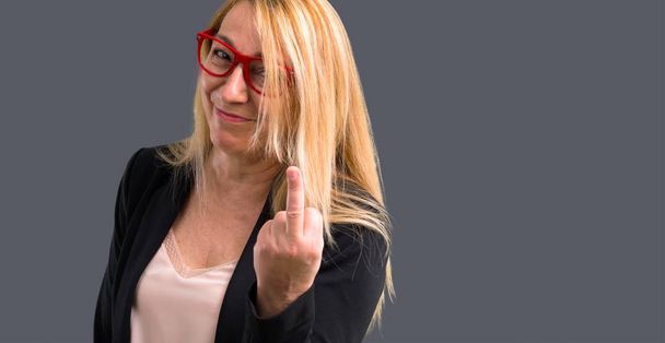 Middle-age blonde business woman with black jacket making horn gesture. Negative expression on isolated grey background - Φωτογραφία, εικόνα