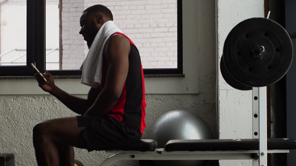 african american sportsman using smartphone after training at gym in slow motion - Filmagem, Vídeo