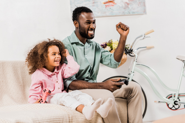 Afrikkalainen amerikkalainen isä ja tytär pelaa videopeliä olohuoneessa
 - Valokuva, kuva