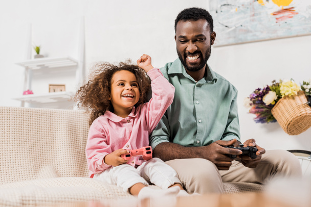 Afrikanisch-amerikanischer Vater und Tochter spielen Videospiel mit Steuerknüppeln im Wohnzimmer - Foto, Bild