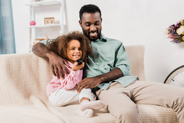 africano americano papá abrazando hija mientras viendo televisión en sala de estar
 - Foto, Imagen