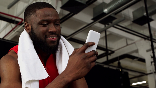 χαμογελώντας αφροαμερικάνος αθλητής χρησιμοποιώντας smartphone μετά την προπόνηση στο γυμναστήριο σε αργή κίνηση - Πλάνα, βίντεο