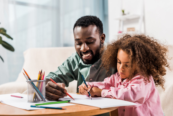 close up view of african american father helping daughter with drawing in living room - Foto, immagini