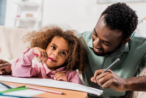 african american man drawing with daughter in living room - Фото, зображення