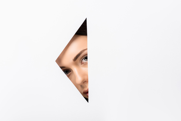 beautiful young woman looking at camera through hole on white   - Photo, Image