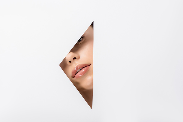 attractive young woman looking at camera through hole on white  - Foto, Imagem