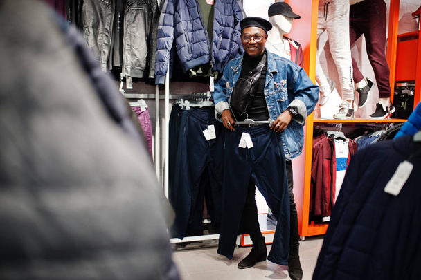 Stylish casual african american man at jeans jacket and black beret at clothes store looking on new sport pants. - Foto, immagini