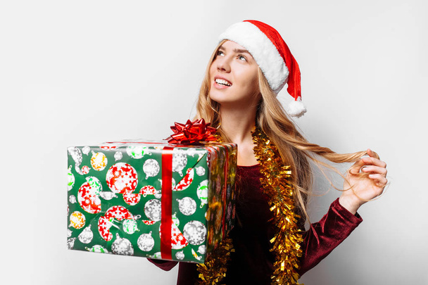 Pensive girl in a hat of Santa Claus, in her hands - Christmas gifts. On a white background - Фото, зображення