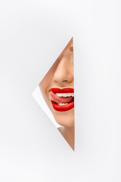 cropped shot of girl licking lips through hole on white - Foto, Bild