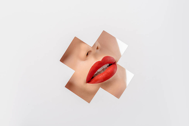cropped shot of young woman with red lips through cross shaped hole on white - Fotografie, Obrázek