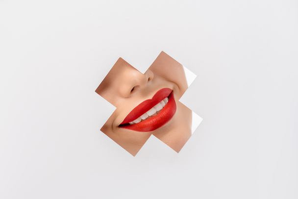 cropped shot of smiling young woman with red lips through cross shaped hole on white - Foto, afbeelding