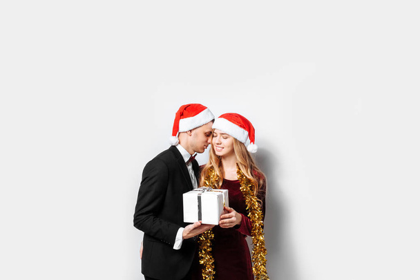 An elegant pair of lovers in Santa Claus hats celebrating the New Year and giving each other Christmas presents. on a white background - Foto, Imagen