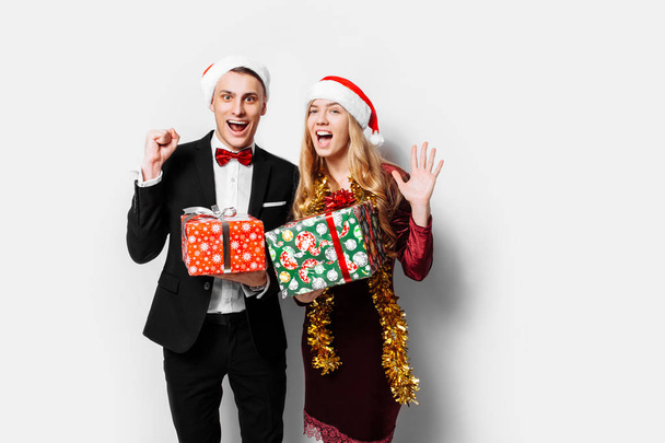 A stunned pair of lovers in Santa Claus hats celebrating the new year and giving each other Christmas presents. on a white background - 写真・画像