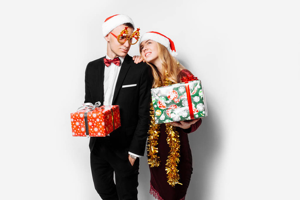 Una feliz pareja de amantes, con sombreros de Papá Noel, celebra el Año Nuevo, con regalos de Navidad en sus manos. Sobre un fondo blanco
. - Foto, imagen