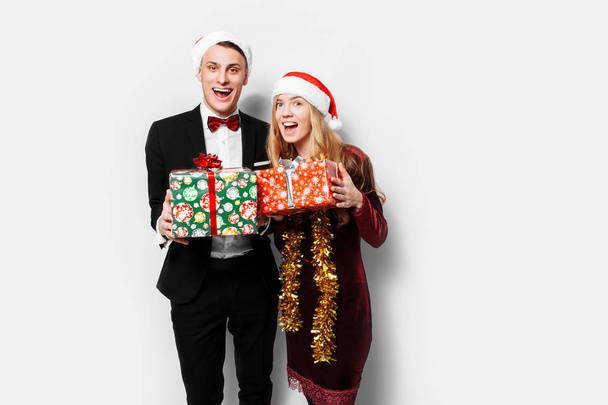 A stunned pair of lovers in Santa Claus hats celebrating the new year and giving each other Christmas presents. on a white background - Foto, imagen