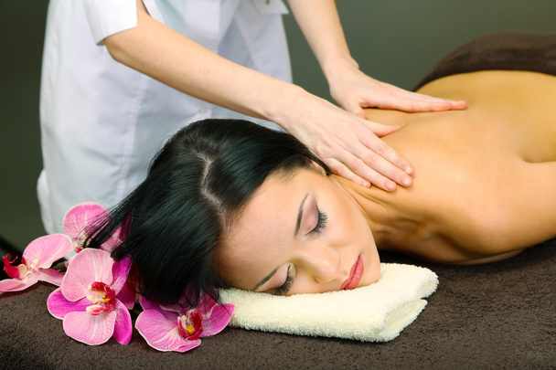 Beautiful young woman in spa salon getting massage with spa stones, on dark background - Фото, зображення