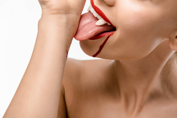 cropped shot of naked girl with vampire teeth licking blood from hand isolated on white - Photo, Image