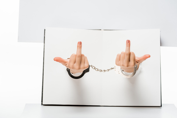 cropped shot of female hand in handcuffs showing middle fingers through holes on white - Fotoğraf, Görsel