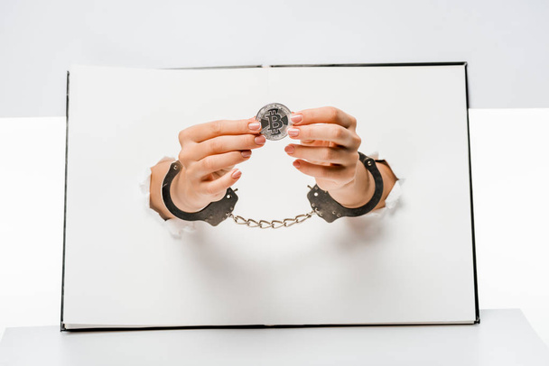 cropped shot of woman in handcuffs holding bitcoin through holes on white  - Φωτογραφία, εικόνα