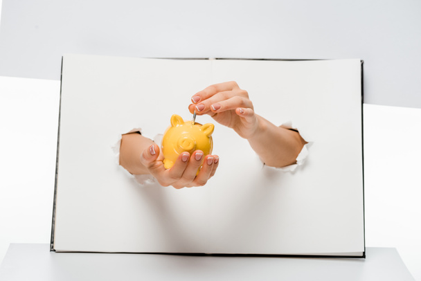 cropped shot of woman putting coin into yellow piggy bank through holes on white  - Photo, image