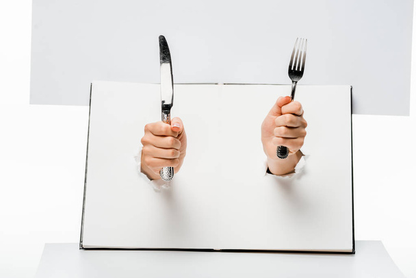 partial view of woman holding fork and knife through holes on white - Foto, immagini