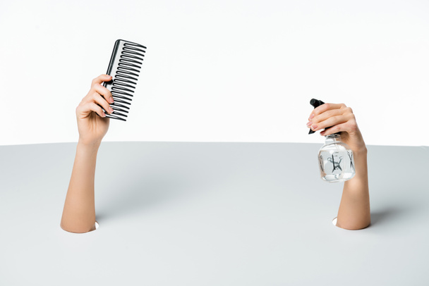 cropped shot of woman holding comb and spray bottle through holes on white - Valokuva, kuva