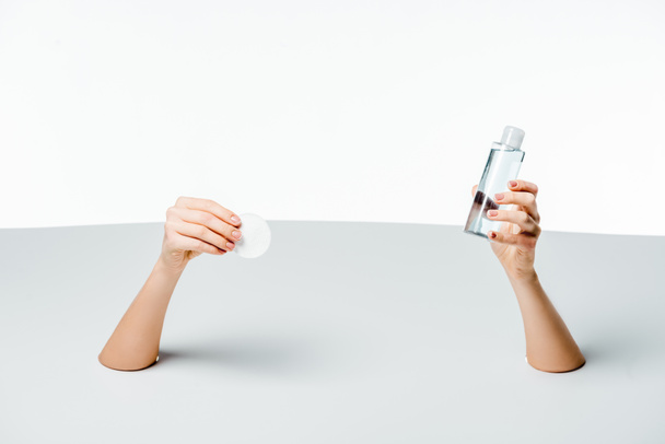 cropped shot of woman holding cotton pad and makeup remover through holes on white - Photo, Image