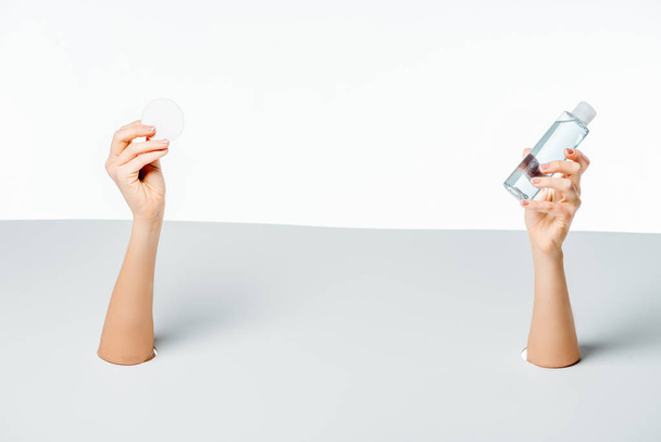 cropped shot of woman holding cotton pad and lotion through holes on white - Photo, image