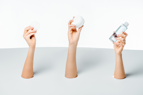 cropped shot of women holding cream, lotion and cotton pad through holes on white - 写真・画像