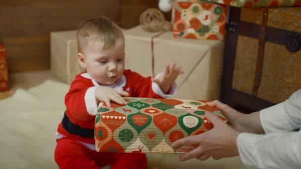 Amazing looked of woman mom giving a gift to her excited cute little boy or girl that clapping her hands near a decorated Christmas tree and gift - Кадри, відео
