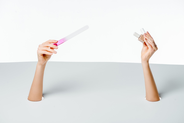 partial view of woman holding nail file and polishes through holes on white  - Foto, afbeelding