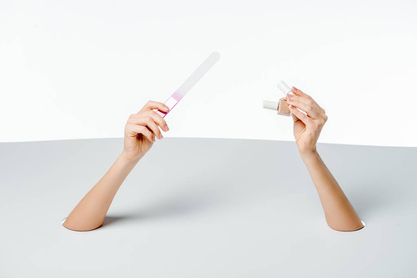 cropped shot of woman holding nail file and polishes through holes on white  - Photo, image
