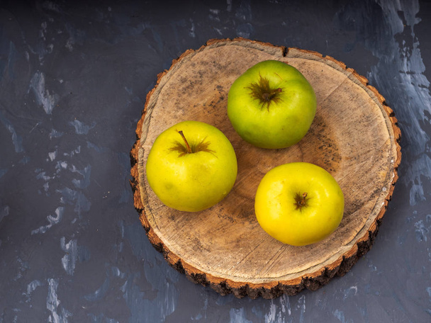 Drie groene gouden appels op een houten plaat, close-up. Grijze achtergrond, close-up. - Foto, afbeelding