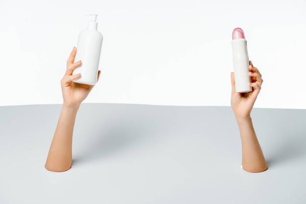 partial view of woman holding beauty products through holes on white    - Foto, afbeelding