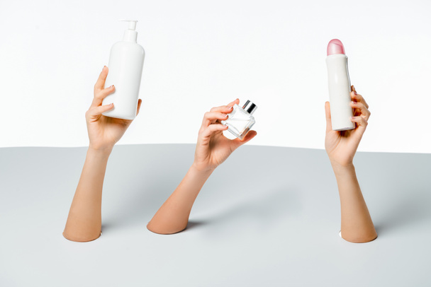 partial view of women holding beauty products through holes on white    - Photo, Image
