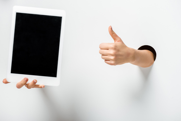 cropped image of woman holding tablet with blank screen through holes and showing thumb up on white - Foto, Imagen