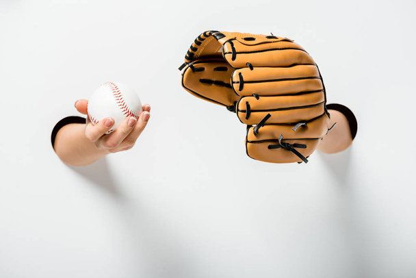 oříznutý obraz ženy držící baseballovou rukavici a míč skrz otvory na bílém - Fotografie, Obrázek