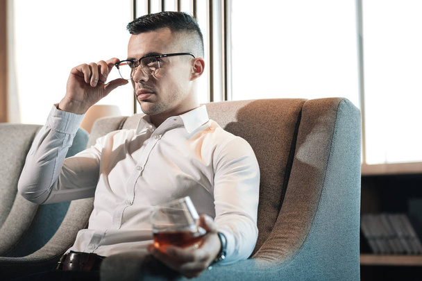 Young dark-haired businessman feeling rested while drinking whisky - Fotoğraf, Görsel