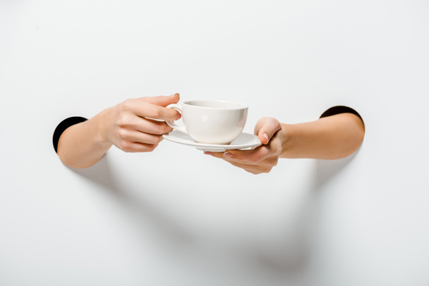cropped image of woman holding cup of coffee and plate through holes on white - Foto, Imagen