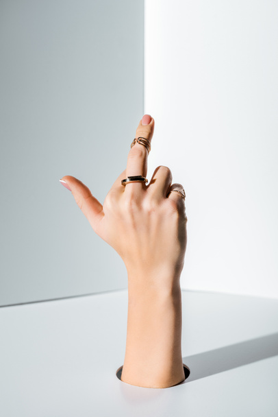 περικομμένη εικόνα δείχνει γυναίκα μεσαίο δάχτυλο με τα δαχτυλίδια μέσα από οπή στο λευκό - Φωτογραφία, εικόνα