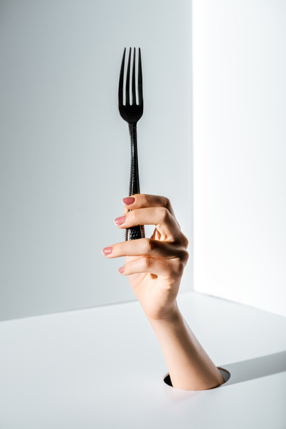cropped image of woman holding fork in hand through hole on white - Фото, зображення