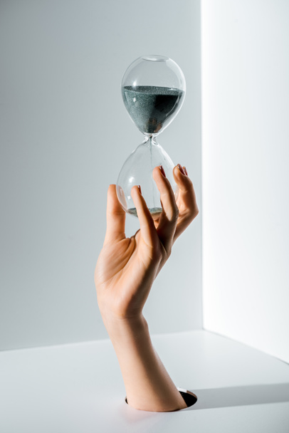 cropped image of woman holding hourglass with grey sand in hand through hole on white - Фото, зображення