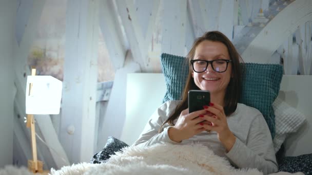 Жінка в окулярах лежить в ліжку і використовує смартфон перед сном
 - Кадри, відео