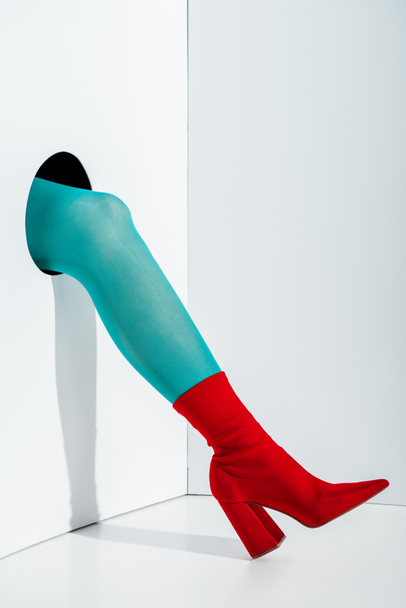 cropped image of woman showing leg in turquoise tights and red shoe in hole on white - Valokuva, kuva