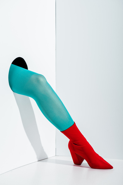 cropped image of girl showing leg in stylish turquoise tights and red shoe in hole on white - Fotó, kép