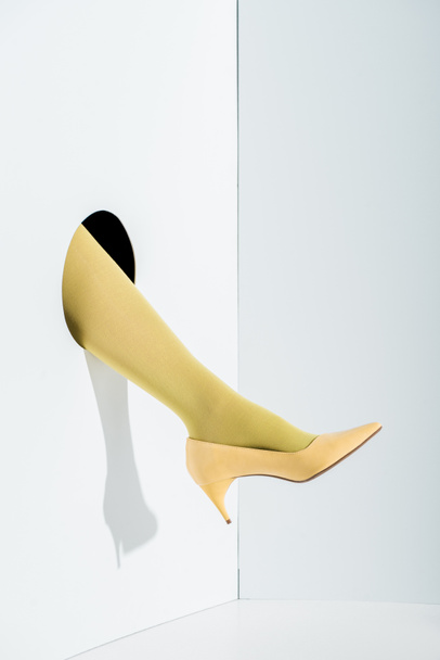 cropped image of girl showing leg in stylish yellow tights and high heel in hole on white - Foto, immagini