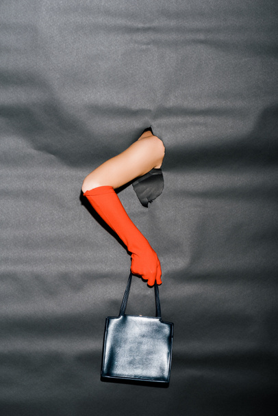 imagem cortada de mulher mostrando mão em luva laranja e bolsa preta através de papel preto
 - Foto, Imagem