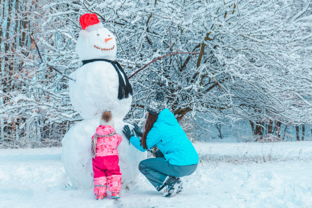 kış döneminde dışında oynarken kızı annesiyle. kardan adam kavram yapma - Fotoğraf, Görsel
