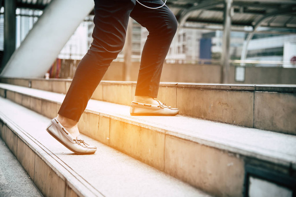 Close up legs of traveling people walking on stepping up stair in modern city. Sneakers and jeans elements. Business and travel concept. City lifestyle and working people theme. Rush hours theme. - Photo, image
