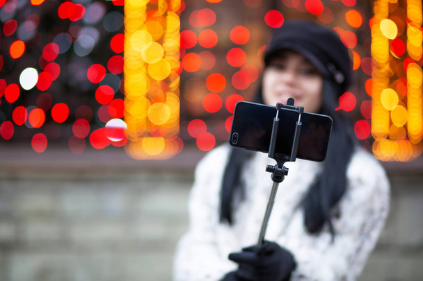 Attractive brunette woman wearing cap, taking self portrait at the street with blurred lights. Empty space - Foto, Bild